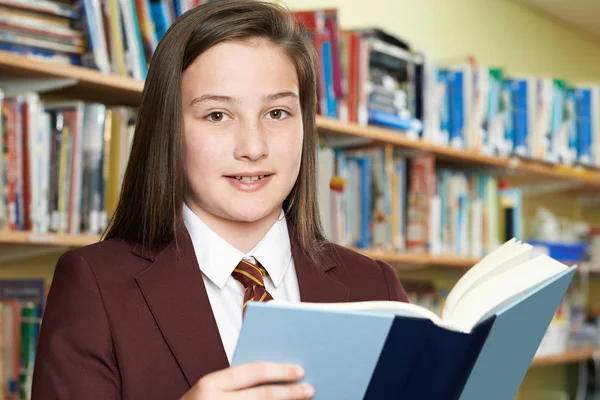 Flicka klädd skola enhetlig läsebok i biblioteket — Stockfoto