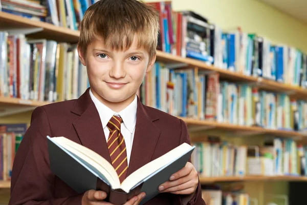 Pojke som bär skola enhetlig läsebok i biblioteket — Stockfoto