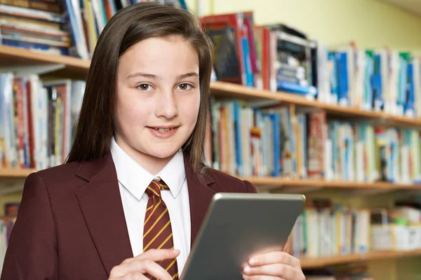 Menina vestindo uniforme escolar usando tablet digital na biblioteca — Fotografia de Stock