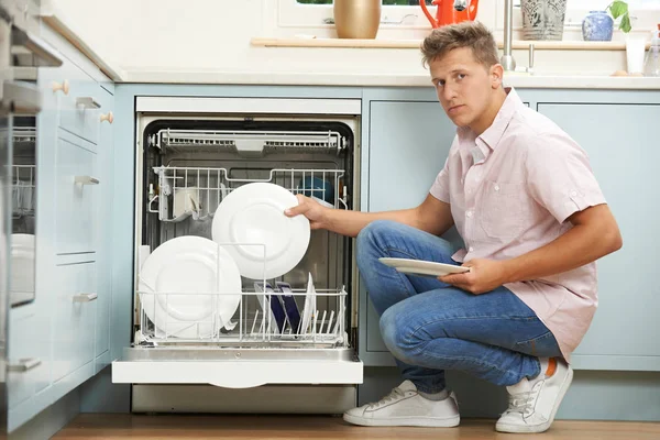 Homem entediado Carregando máquina de lavar louça na cozinha — Fotografia de Stock