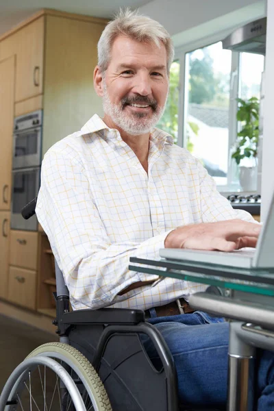 Homem com deficiência em cadeira de rodas usando laptop em casa — Fotografia de Stock