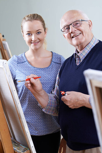 Senior Man Attending Painting Class With Teacher
