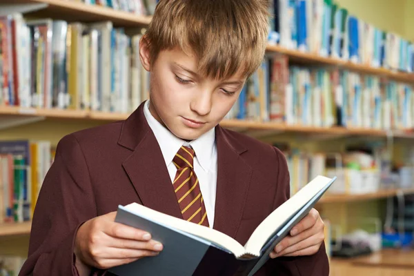 Pojke som bär skola enhetlig läsebok i biblioteket — Stockfoto