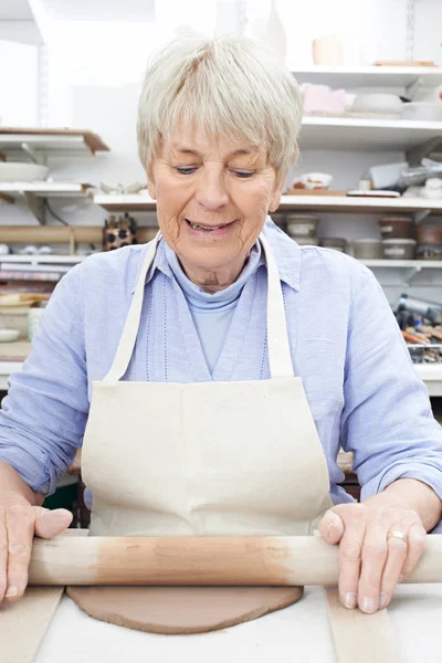 Старшая женщина выкатывает глину в керамической мастерской — стоковое фото