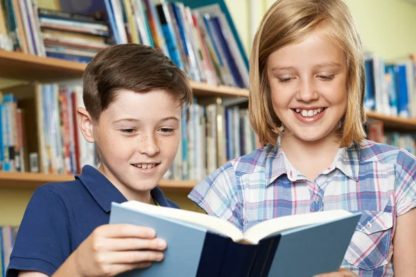 Дві школярі читають книгу в бібліотеці — стокове фото