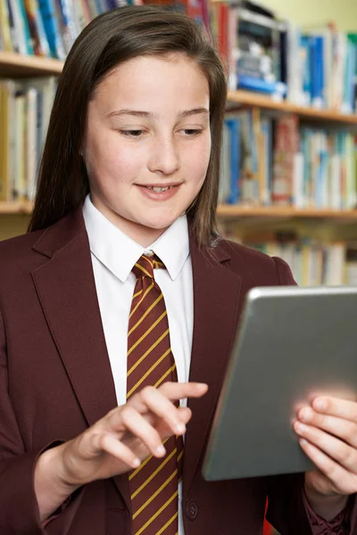 Chica vistiendo uniforme escolar usando tableta digital en la biblioteca —  Fotos de Stock