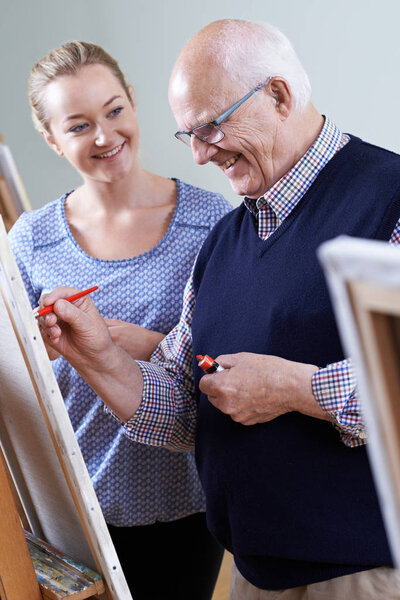 Senior Man Attending Painting Class With Teacher