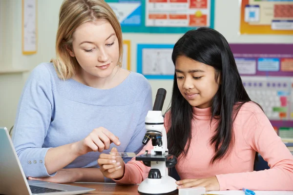 Profesor con estudiante femenino usando microscopio en clase de ciencias —  Fotos de Stock