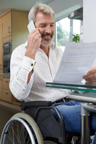 Человек в инвалидной коляске звонит во время чтения письма — стоковое фото
