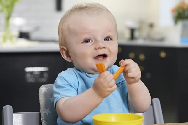 Feliz niño sentado en la mesa comiendo zanahorias frescas —  Fotos de Stock