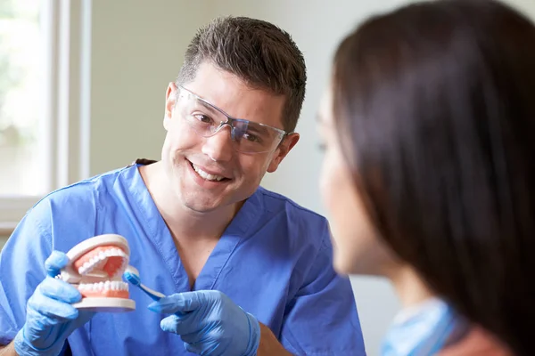 Dentysta, wykazując poprawne użycie szczoteczki do kobiety klienta — Zdjęcie stockowe