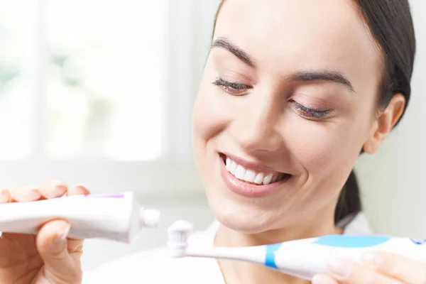 Жінка стискає зубну пасту на електричну зубну щітку у ванній — стокове фото