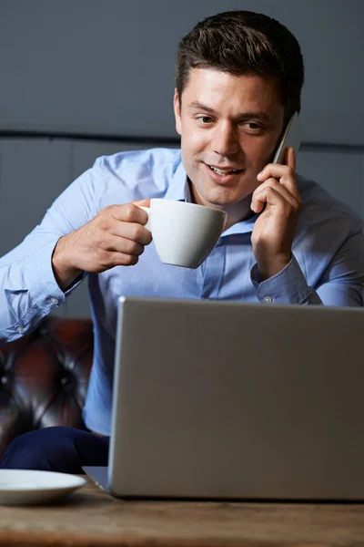 Uomo d'affari che parla sul telefono cellulare che lavora sul computer portatile in Interne — Foto Stock