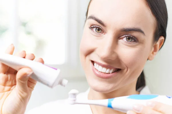 Mujer apretando pasta de dientes en cepillo de dientes eléctrico en el baño — Foto de Stock