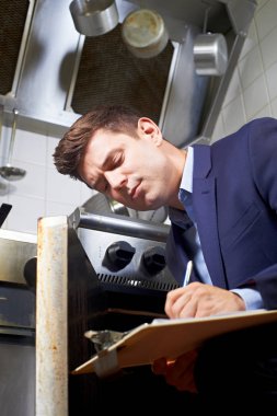 Health Inspector Looking At Oven In Commercial Kitchen clipart