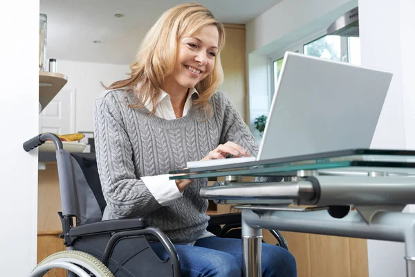 Evde dizüstü bilgisayar kullanan tekerlekli sandalyedeki engelli kadın. — Stok fotoğraf