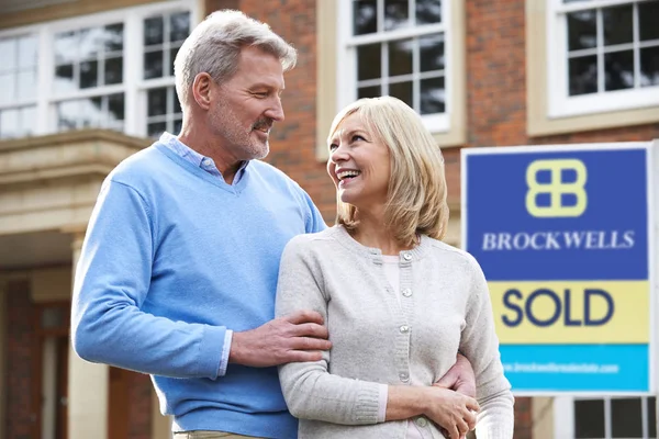 Pareja madura feliz de pie fuera de casa con signo vendido — Foto de Stock