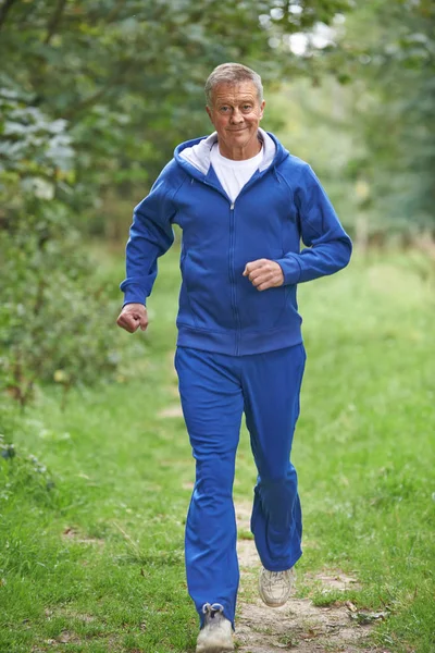 Uomo anziano in tuta che corre attraverso la campagna — Foto Stock