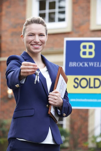 Femme agent immobilier debout à l'extérieur de la propriété résidentielle détenant la clé — Photo