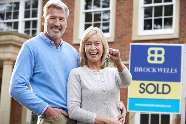 Älteres Ehepaar hält Schlüssel für neues Eigenheim an verkauftem Schild — Stockfoto