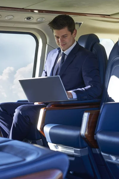 Бизнесмен, работающий над ноутбуком в кабине вертолета во время полета — стоковое фото