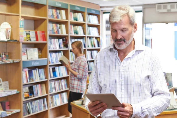 Ο ιδιοκτήτης του βιβλιοπωλείου αρσενικό χρησιμοποιώντας ψηφιακό Tablet με πελάτη Backg — Φωτογραφία Αρχείου