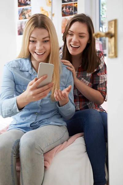 Sonriente adolescente con amigo leyendo el mensaje de texto en el dormitorio — Foto de Stock