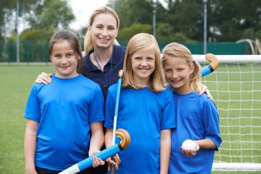 Okuldaki bayan koçla kız hokey takımının portresi.