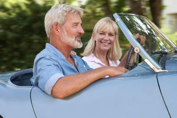 Pareja madura disfrutando de un viaje por carretera en un clásico coche deportivo abierto — Foto de Stock