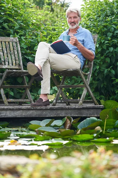 Portrait Of Mature Man Relaxing In Garden Reading Book On Jetty — Stock Photo, Image