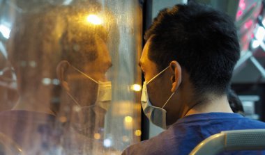 Taichung, Tayvan - 17 Nisan 2020: Bir adam gece boyunca bir otobüsün içinde maske takıyor ve penceresindeki yansıması endişe ve endişe duygularını gösteriyor