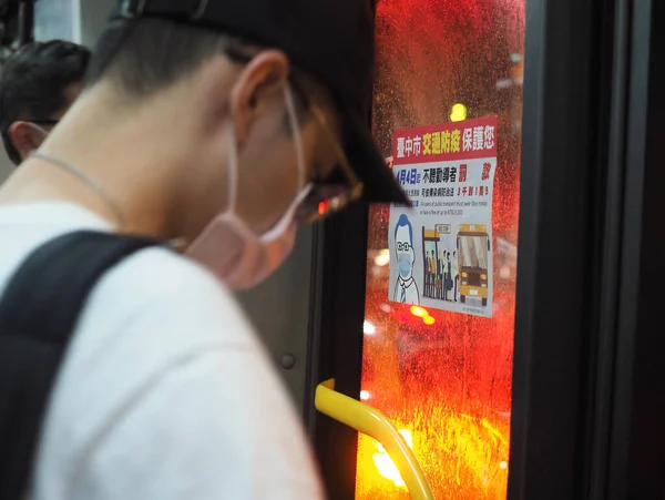 Taichung, Tayvan - 17 Nisan 2020: Pencerede salgın önleme ilanı olan otobüs kapısının yanında maske takan bir adam, toplu taşıma araçlarının kullanıcılarının maske takması veya para cezasına çarptırılması gerektiğini bildirdi