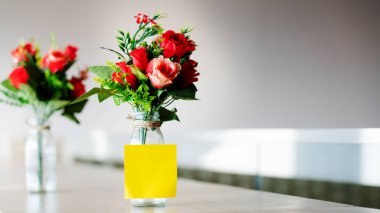 Ahşap bir masanın üzerine yerleştirilmiş cam bir şişedeki kırmızı plastik güller. Düğün süslemeleri, sevgililer günü, ev dekorasyonları ya da ofis. Sahte çiçek ihraç işi yapıyor. Boşluğu kopyala