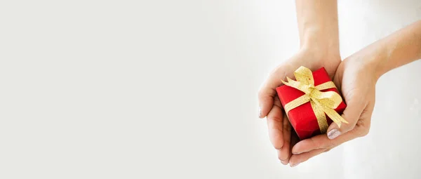 Elinde altın kurdeleli kırmızı bir hediye kutusu olan eli kapat Sevgililer Günü 'nde sevgiline hediye ver. Ya da doğum günleri, Noel ve Mutlu Yıllar gibi önemli festivaller. Teslimat konsepti