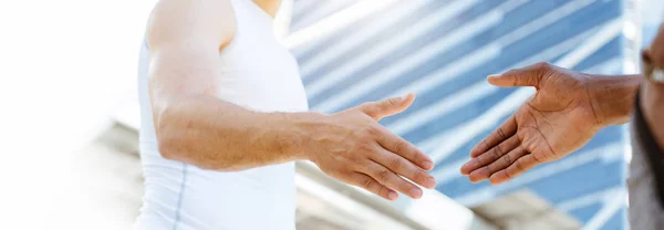 Beyaz spor kıyafetleri giymiş, şehirde bir spor salonunda duran sporcu bir arkadaşla el sıkışmak üzere olan bir erkek sporcunun elini yakın plan çekiyoruz. Sağlığınıza dikkat etmeyi kabul edin. Boşluğu kopyala