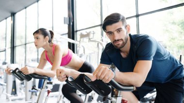 Erkekler ve kadınlar spor giyer spor kıyafetleri giyer, spor salonunda bisiklet sürerler, sağlık hizmeti maksadıyla. Dar kaslarla vücudu sağlıklı yapmak ve ağırlığı azaltmak için bisiklete binmek. Spor ve sağlık konsepti
