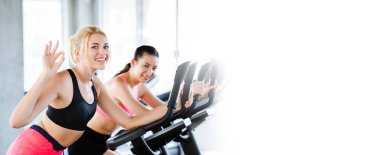 Spor kıyafetleri giyen kadınlar spor yapıyor, spor salonunda elektrikli bisiklet çeviriyor sağlık için güzel bir şekle sahip oluyorlar ve kasların gevşemesini sağlıyorlar. afiş arkaplanına boşluk kopyala.