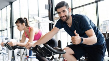 Erkekler ve kadınlar spor giyer spor kıyafetleri giyer, spor salonunda bisiklet sürerler, sağlık hizmeti maksadıyla. Dar kaslarla vücudu sağlıklı yapmak ve ağırlığı azaltmak için bisiklete binmek. Spor ve sağlık konsepti