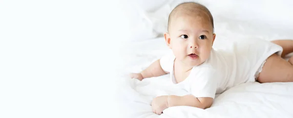 Yakışıklı Asyalı bebek yatak odasındaki temiz beyaz yatakta. Yeni doğan bebek rahat hissediyor, yatakta mutlu. Küçük çocuklar için çocuk odası. Çocuğun fiziksel gelişimi. Kopyalama alanı olan pankart