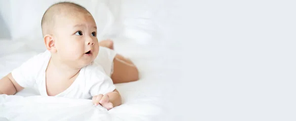 Yakışıklı Asyalı bebek yatak odasındaki temiz beyaz yatakta. Yeni doğan bebek rahat hissediyor, yatakta mutlu. Küçük çocuklar için çocuk odası. Çocuğun fiziksel gelişimi. Kopyalama alanı olan pankart