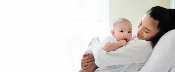 Yeni doğan oğlunu kucaklayan güzel Asyalı annenin portresi. Bebek çok sevimli. Anne çocuk sağlıklıyken mutlu bir şekilde gülümsüyor. Küçük çocuklar için çocuk odası. Kopyalama alanı olan pankart