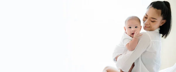 Yeni doğan oğlunu kucaklayan güzel Asyalı annenin portresi. Bebek çok sevimli. Anne çocuk sağlıklıyken mutlu bir şekilde gülümsüyor. Küçük çocuklar için çocuk odası. Kopyalama alanı olan pankart