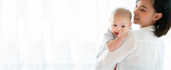 Yeni doğan oğlunu kucaklayan güzel Asyalı annenin portresi. Bebek çok sevimli. Anne çocuk sağlıklıyken mutlu bir şekilde gülümsüyor. Küçük çocuklar için çocuk odası. Kopyalama alanı olan pankart