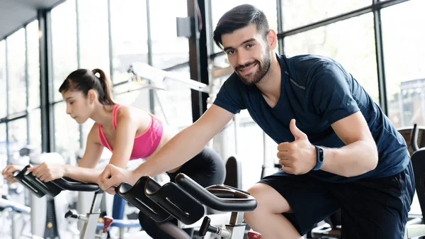 Men and women wear sportswear, workout ride a bike in gym, with the intention of healthcare. Cycling to make body healthy With tight muscles And reduce the weight good. sports and healthcare concept