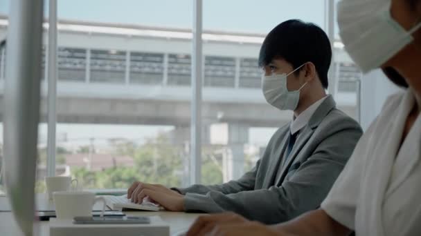 亚洲商人男人和女人戴着防护面具坐在现代化的办公室里工作 使用计算机进行营销信息的工作 别再散播考拉韦病毒了或者是同事的流感 — 图库视频影像