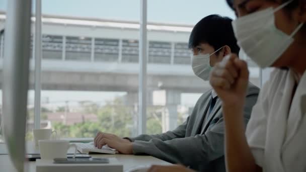 アジアのビジネスマン男性と女性は 現代のオフィスに座って働くために保護マスクを着用してください コンピュータを使用してマーケティング情報に取り組みます コロナウイルスを拡散しないでください または同僚のインフルエンザは — ストック動画