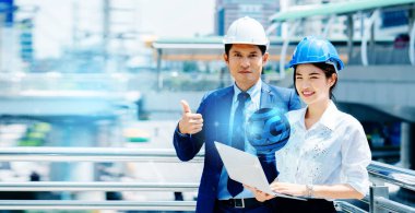 İki Asyalı mühendis iş hakkında konuşuyor. Bilgi bulmak için dizüstü bilgisayar kullanmak, sistematik yapı, 5G teknolojisi. Kask takmak, iş yerindeki kazaları önlemeye yardımcı olur..