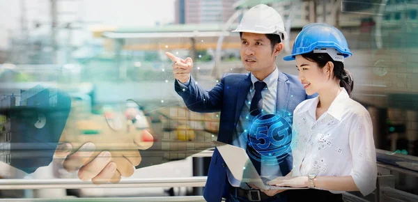 Two Asian people engineers are talking about work. Using a laptop to find information, systematic construction, 5G technology construction. Wearing a helmet helps prevent accidents in the workplace.