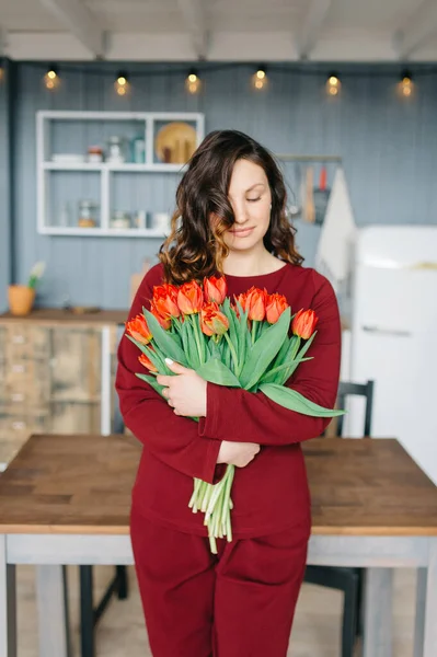 Young woman with a bouquet of tulip flowers staying home. Fashion portrait in the kitchen