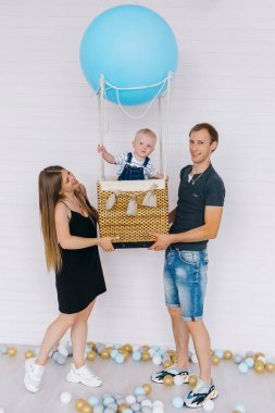 Kotlu küçük bir çocuk mavi bir balonda beyaz bir arka planda ailesiyle birlikte. Aileler oğullarını öpüyor.